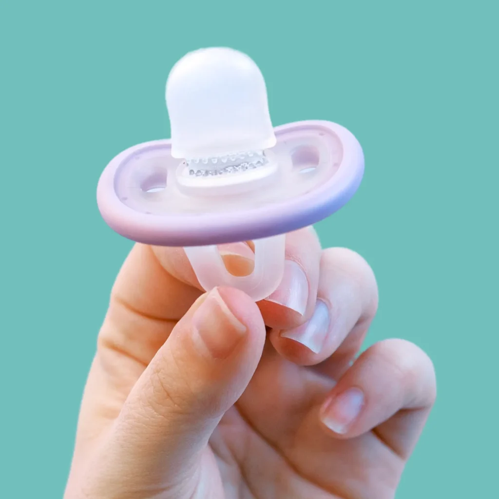 close up of the calm and clean pacifier toothbrush from the side, held by a parent's fingers