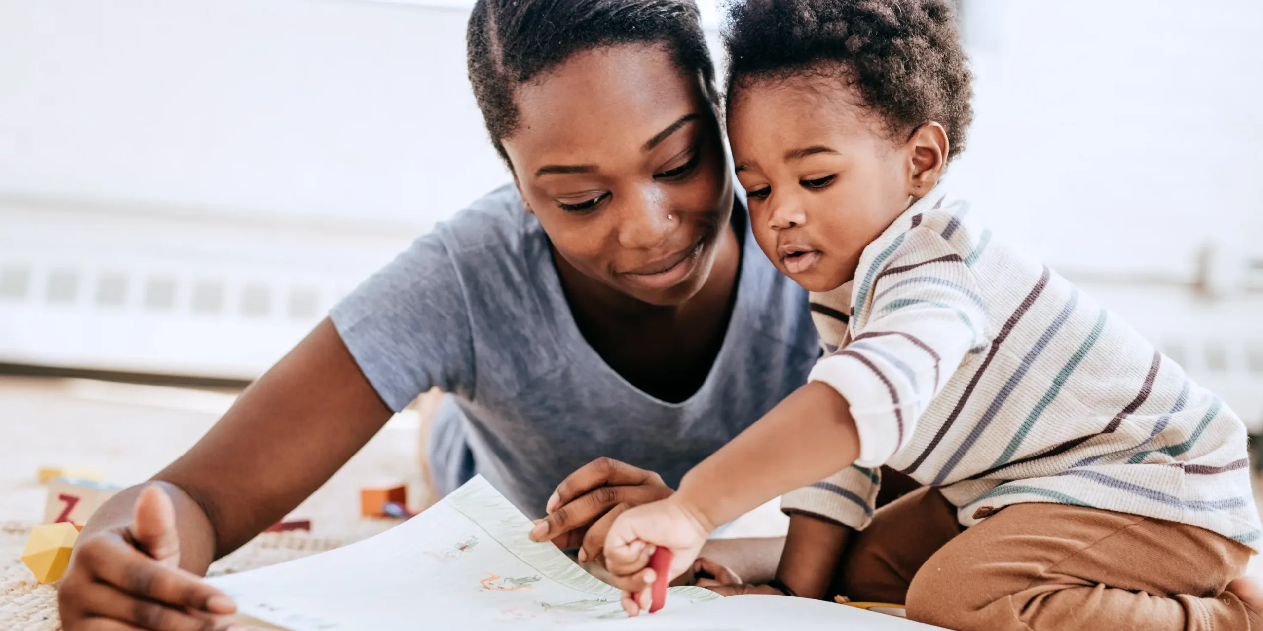 black mother and son engaged in play together drawing with crayons