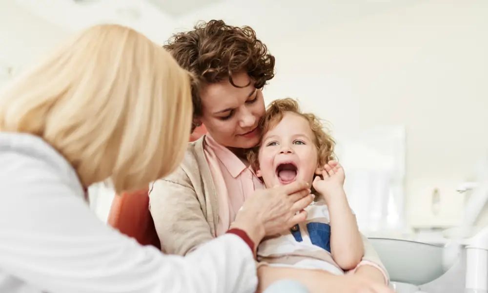 toddler sitting on mothers lap while dentist looks at his baby teeth