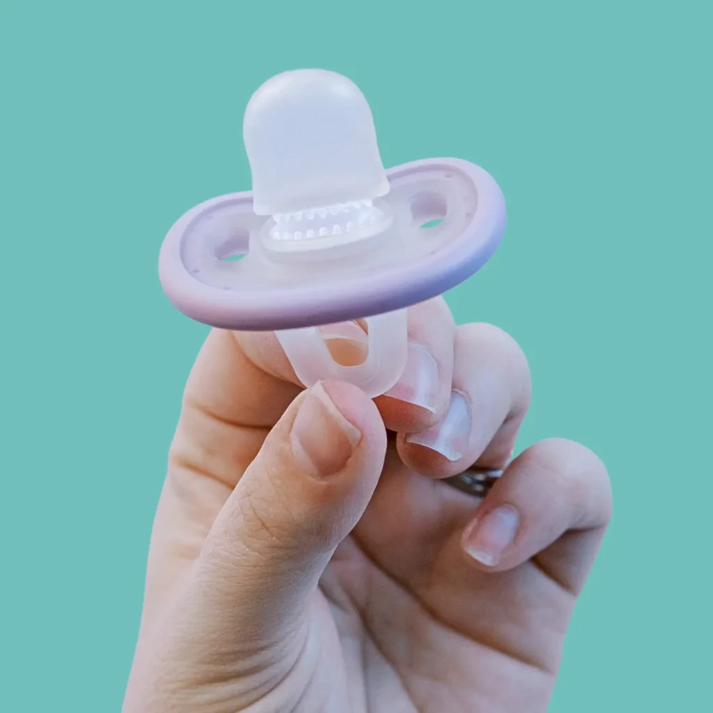 close up of the calm and clean pacifier toothbrush from the side, held by a parent's fingers